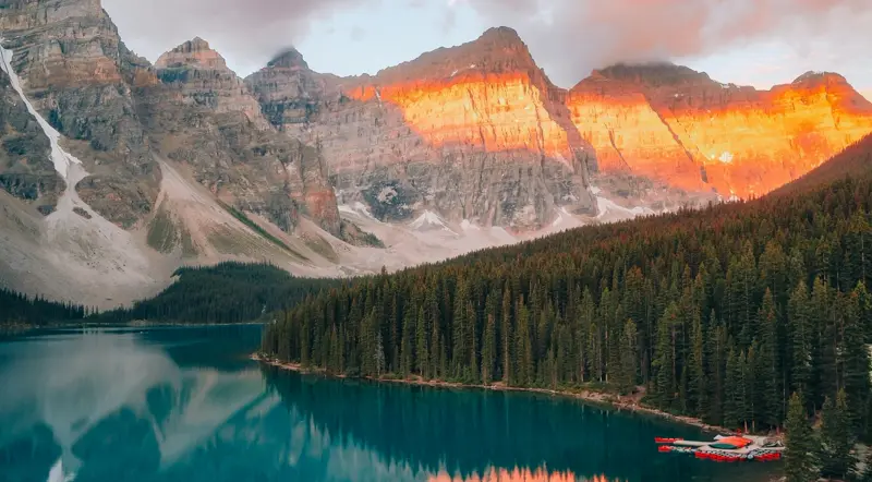 Golden sunrise alpenglow on the peaks above Moraine Lake with canoes at the dock